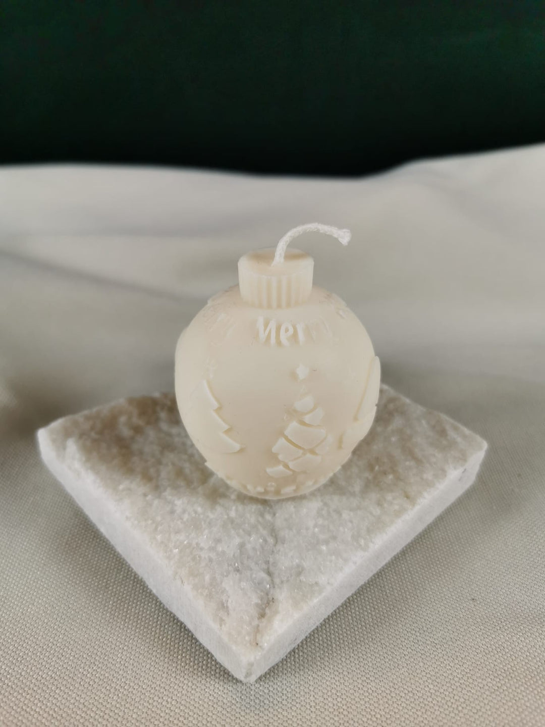 Handgegossene Weihnachtskugel-Kerze aus hellem Rapswachs, mit feiner „Merry Christmas“-Prägung und winterlichen Ornamenten, dekorativ auf Steinplatte präsentiert.