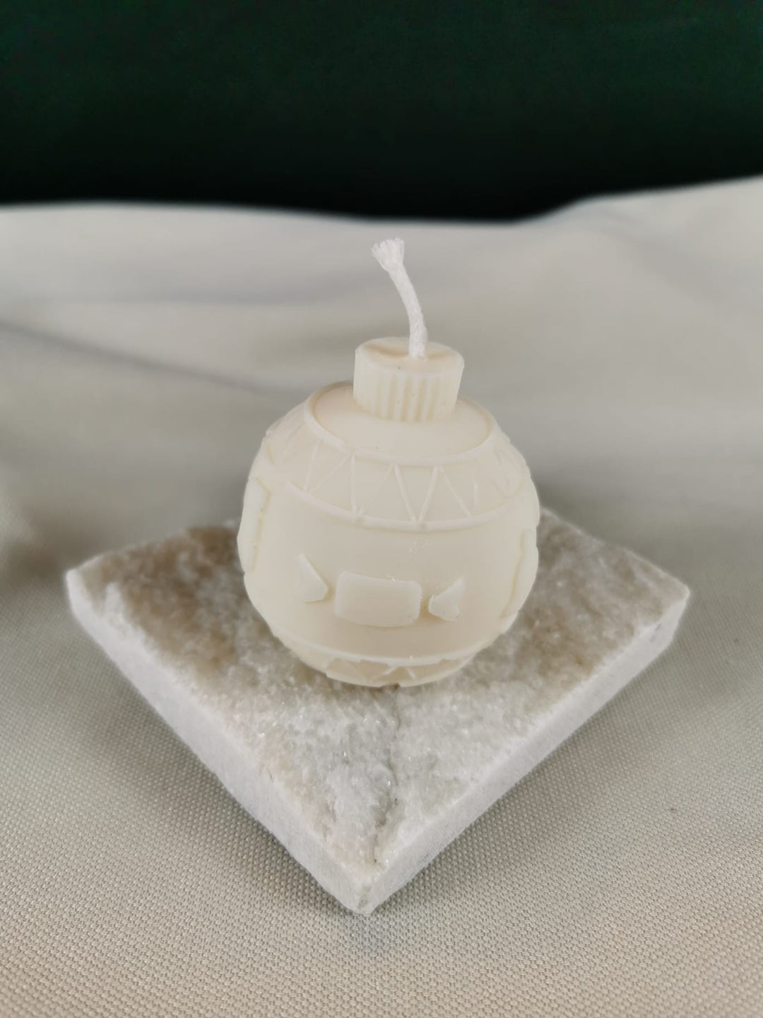 Handgegossene Weihnachtskugel-Figurenkerze aus hellem Rapswachs mit nordischem Muster und glatter Oberfläche, auf einer kristalligen Steinplatte präsentiert.