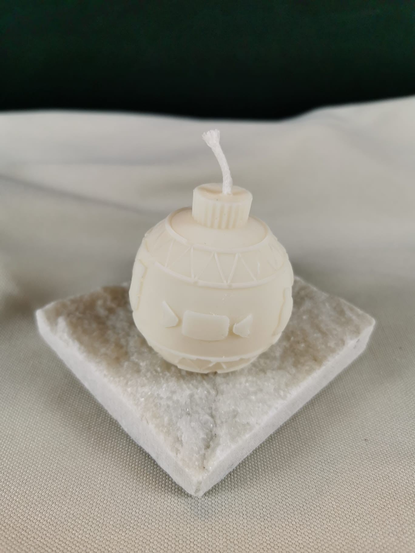 Handgegossene Weihnachtskugel-Figurenkerze aus hellem Rapswachs mit nordischem Muster und glatter Oberfläche, auf einer kristalligen Steinplatte präsentiert.