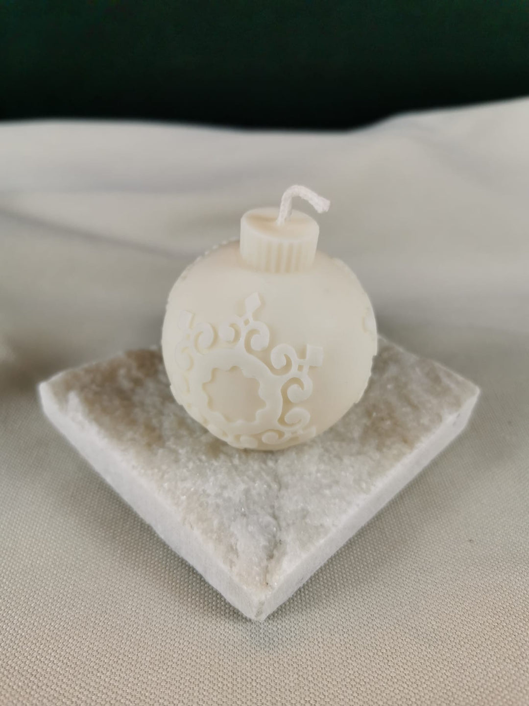 Handgemachte weiße Weihnachtskugel-Kerze mit filigranen Ornamenten aus veganem Rapswachs auf Natursteinplatte