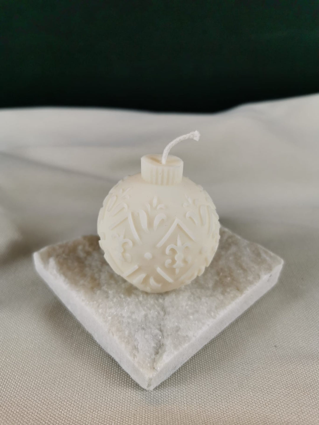 Detailreiche handgegossene Weihnachtskugel-Kerze aus hellem Rapswachs mit ornamentalen Mustern, dekorativ auf Steinplatte präsentiert.