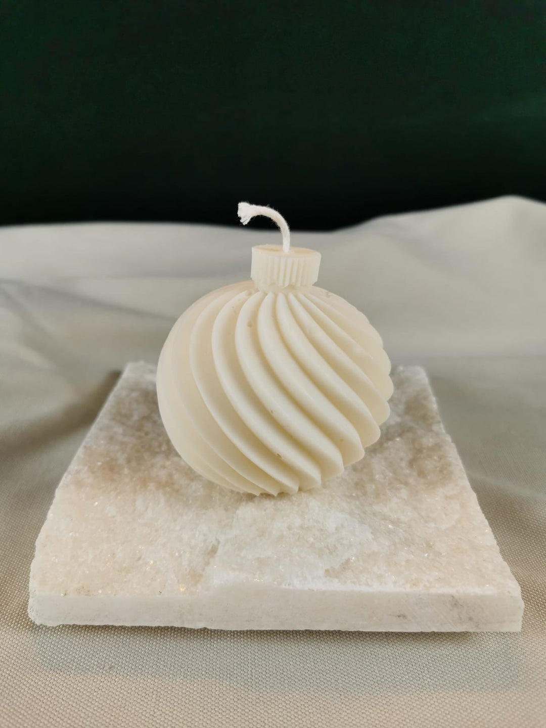 Handgegossene Weihnachtskugel-Kerze aus hellem Rapswachs mit feinem Rillen-Design, auf einer hellen Steinplatte dekorativ präsentiert.