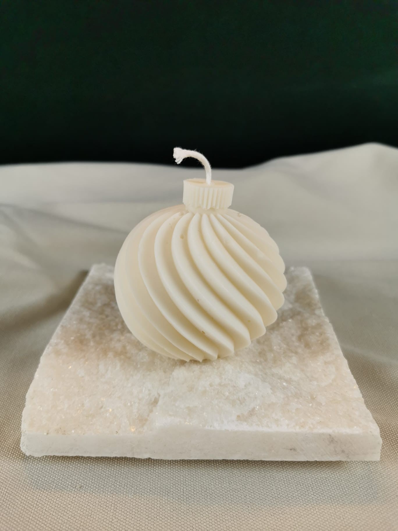 Handgegossene Weihnachtskugel-Kerze aus hellem Rapswachs mit feinem Rillen-Design, auf einer hellen Steinplatte dekorativ präsentiert.