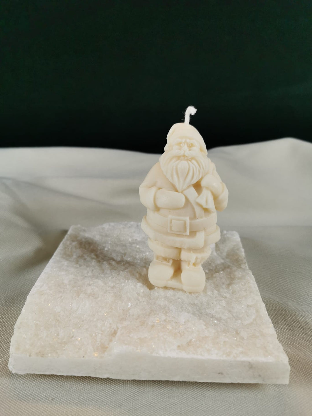 Handgegossene Weihnachtsmann-Figurenkerze aus hellem Rapswachs, detailliert gestaltet und auf einer glitzernden Steinplatte präsentiert.