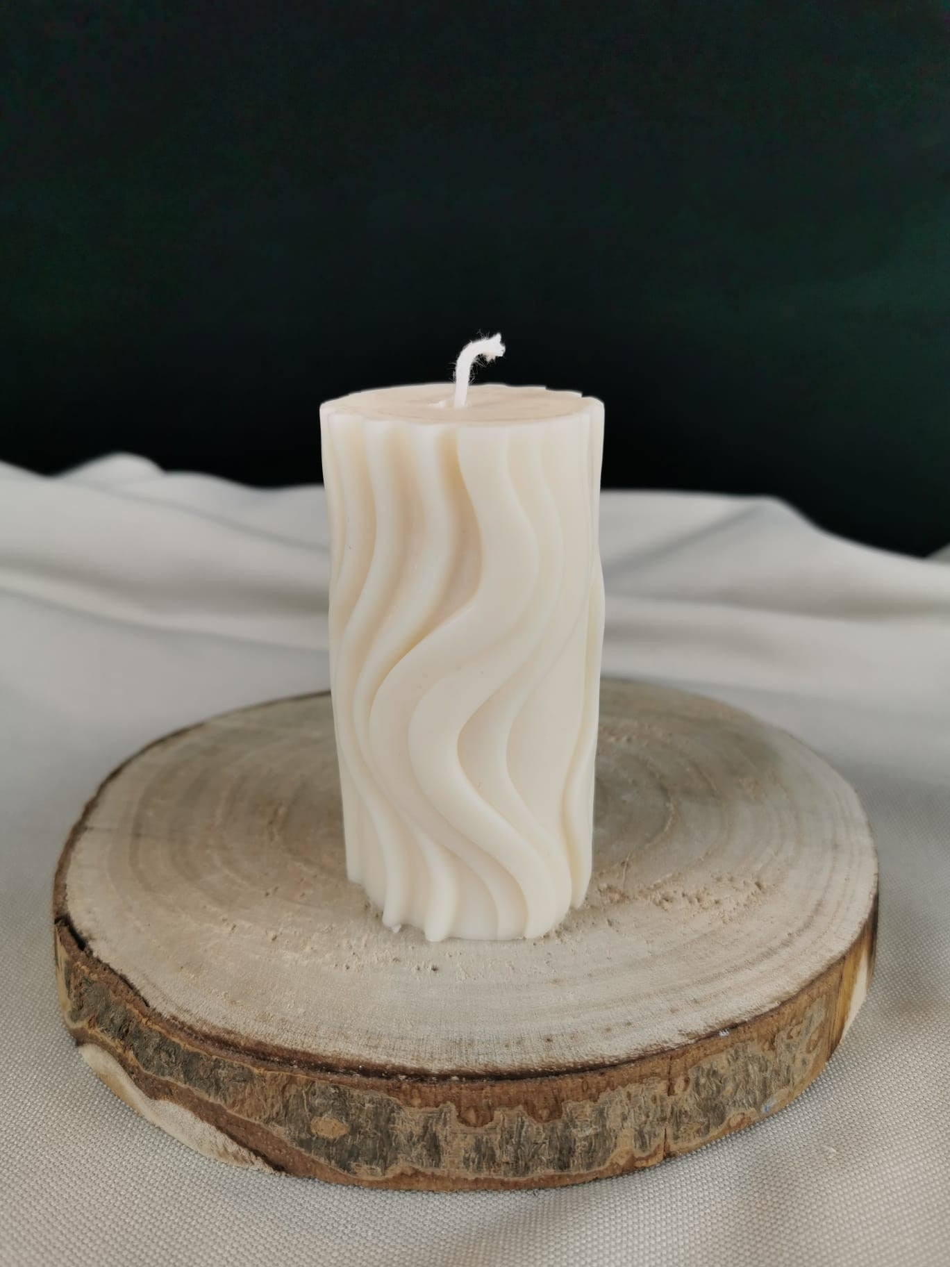 Handgemachte cremefarbene Rapswachskerze mit elegantem Wellenmuster auf einer Holzscheibe, dekorative Designkerze.
