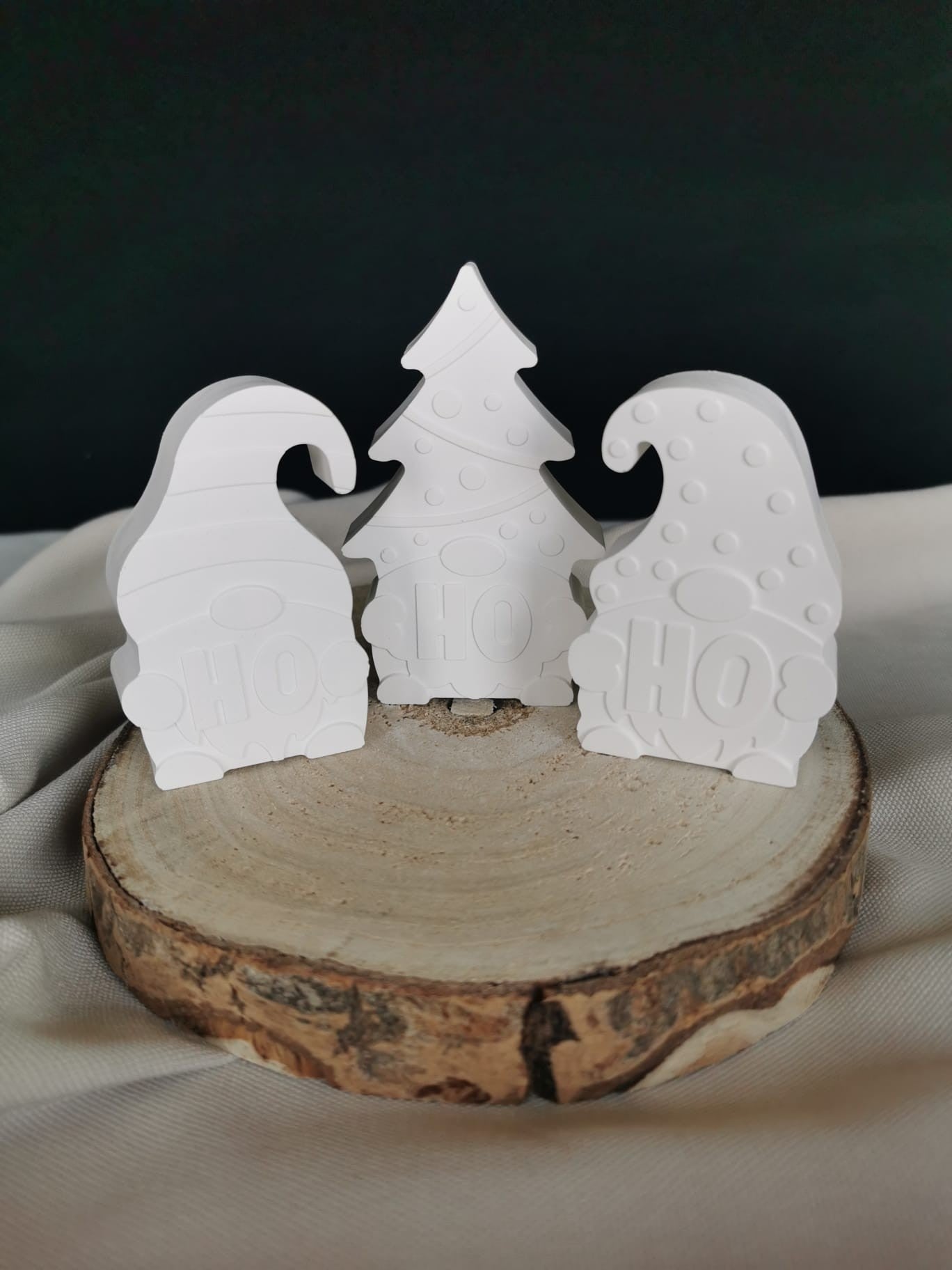 3-teiliges Deko-Set aus weißer Keramik mit zwei Wichteln und einem Tannenbaum mit „HO“-Prägung, auf einem Holzbrett präsentiert.